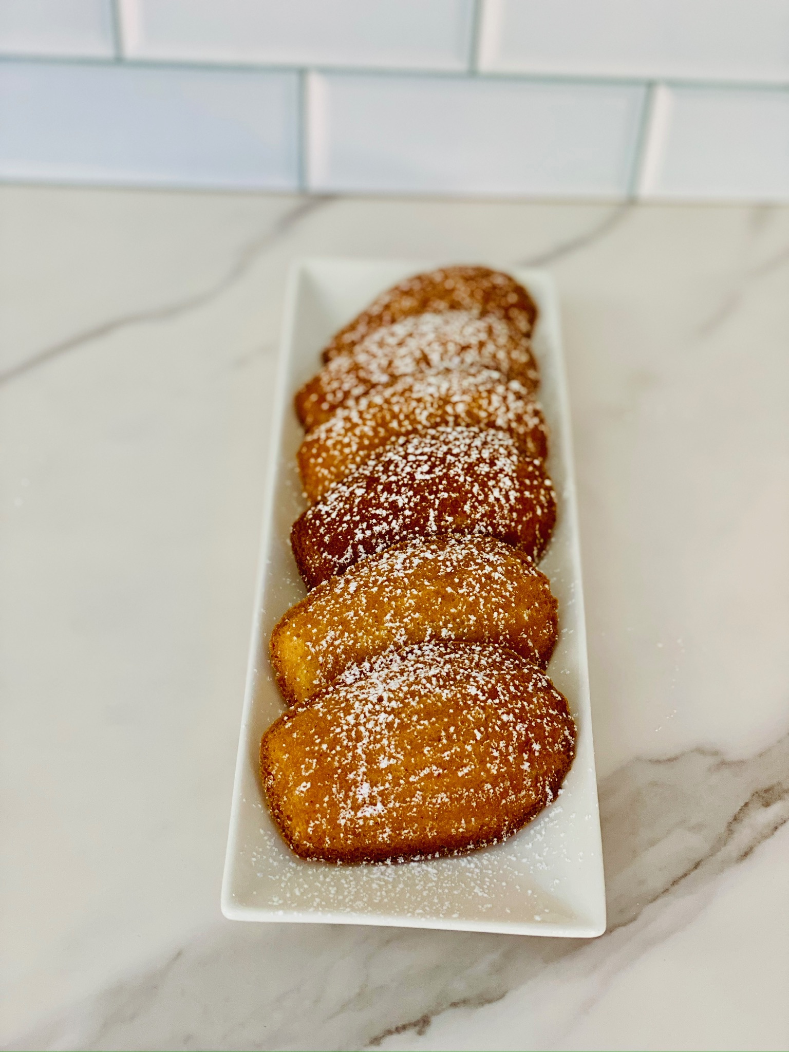 A row of Mochi Maddies madeleines dusted with powdered sugar on a white tray