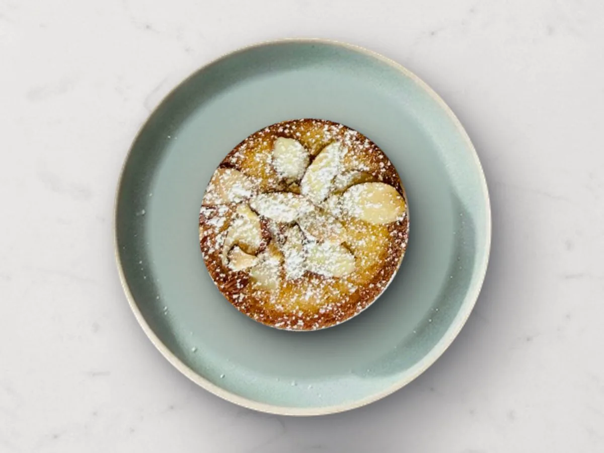 A Classic Butter mochi cake topped with toasted sliced almonds and powdered sugar on a sage plate