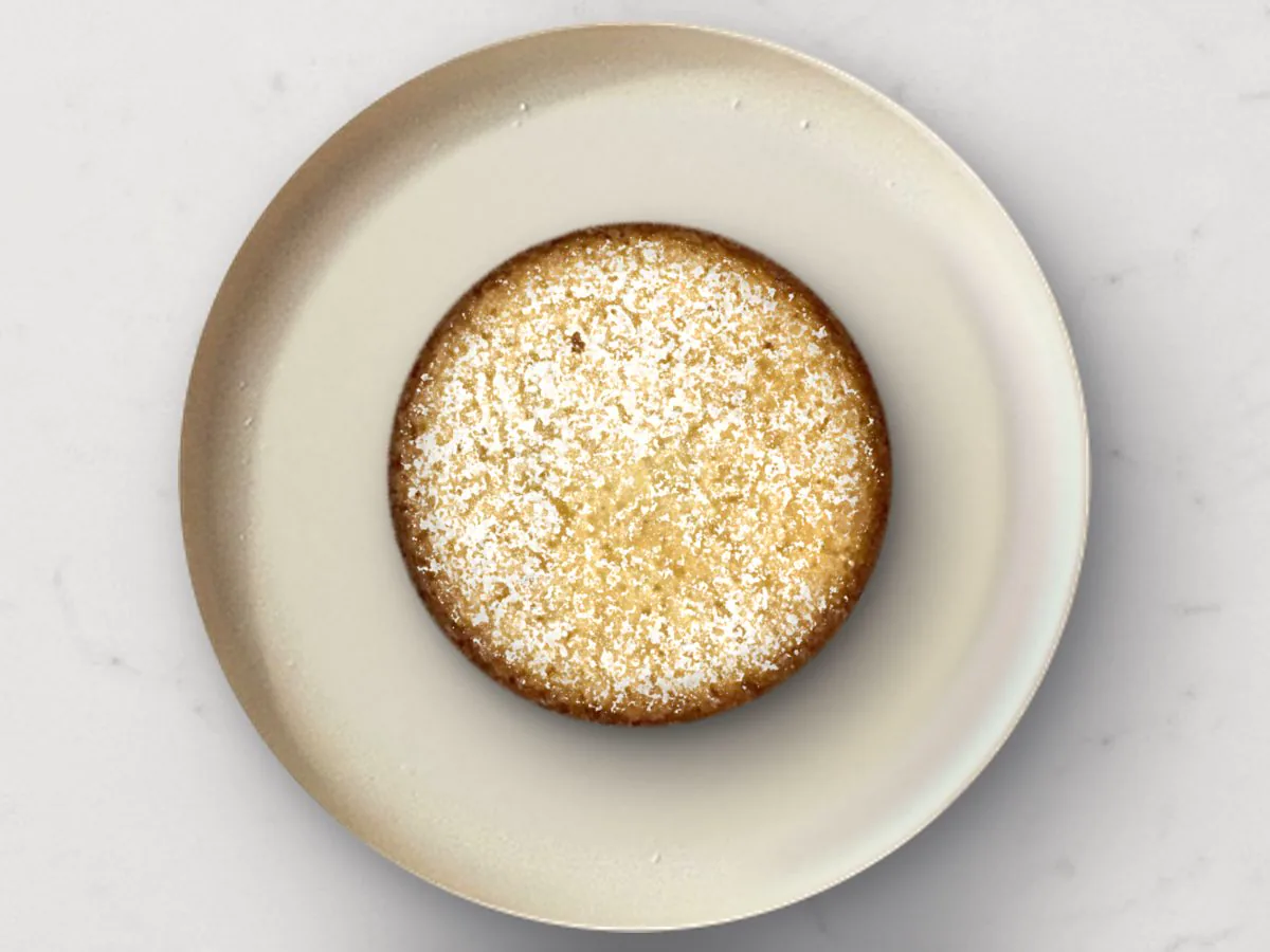 A Classic Butter mochi cake dusted with powdered sugar on a cream plate, white marble, top-down
