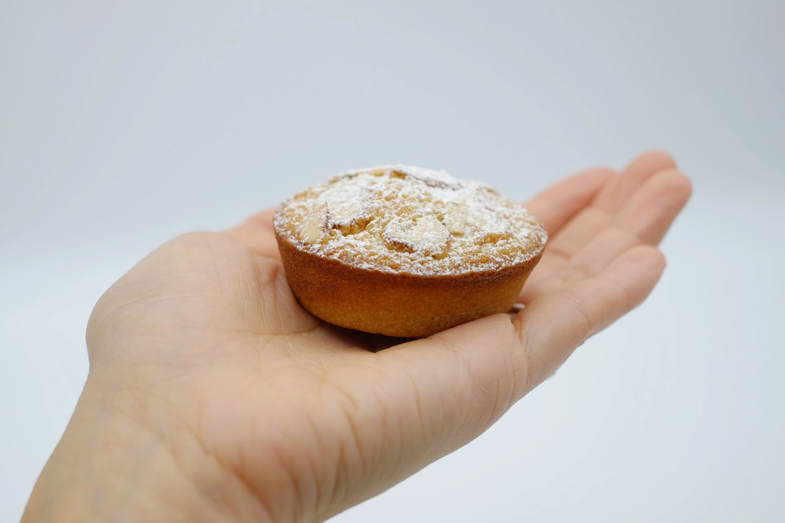 A golden mochi cake with a crisp edge, topped with sliced almonds and powdered sugar, held in one hand